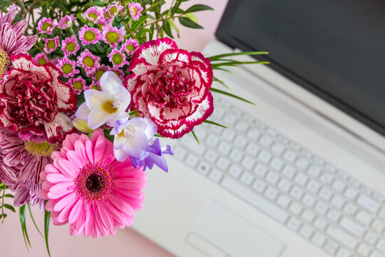 Bouquet of colorful flowers beside a laptop keyboard on a modern desk. Happy remote work combines productivity creativity and wellbeing in a home office.