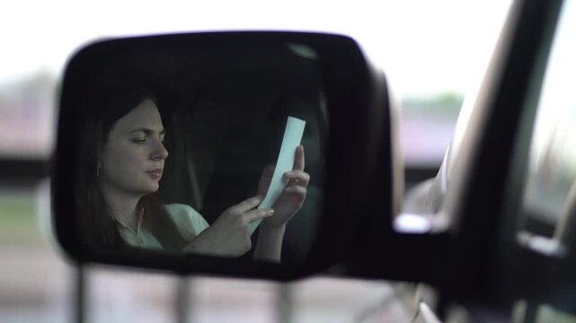A pensive woman in her car studies a paper receipt after expensive purchases. Serious expression reflects budget concerns in realistic lifestyle footage.