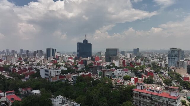 Aerial panoramic view of the Mexico City skyline looking south with modern skyscrapers, drone tracking sideways over the sprawling cityscape under a cloudy blue sky
