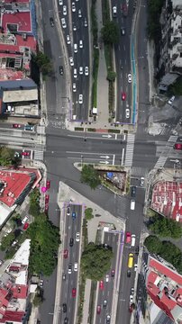 Vertical aerial top-down view of a busy urban intersection and underpass in Mexico City with the drone hovering over flowing traffic and tree-lined medians