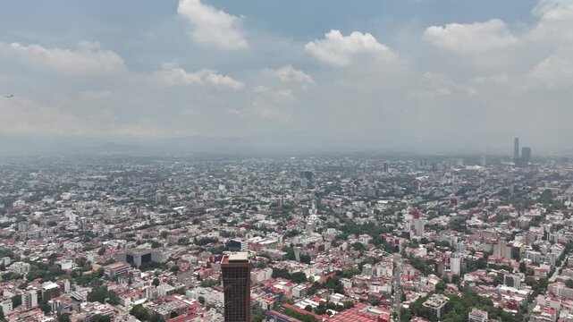 High-altitude panoramic aerial view of the vast Mexico City skyline with the drone panning across the sprawling cityscape under a cloudy blue sky