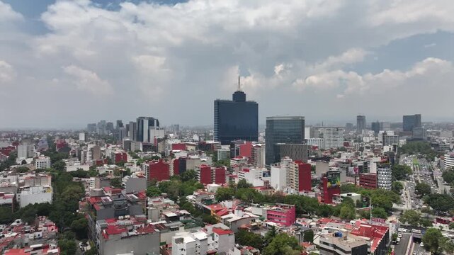 Aerial panoramic view of the Mexico City skyline looking south, drone rotating over sprawling urban buildings under a dramatic cloudy blue sky