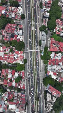 Vertical aerial top-down view of the Viaducto highway in Mexico City with heavy traffic flowing between dense residential neighborhoods and green trees