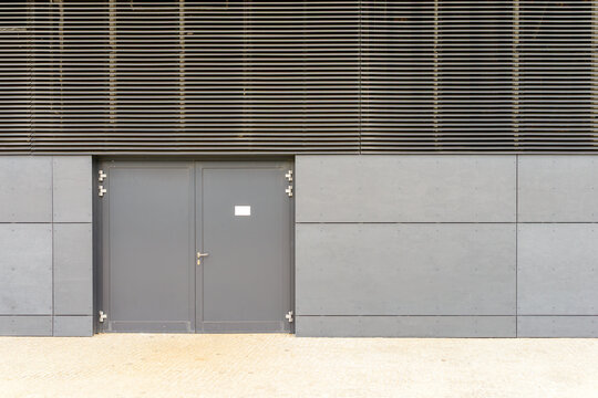 Modern grey facade with closed double entrance doors and industrial cladding panels on a contemporary building exterior
