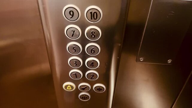 Elevator control panel with numbered buttons. The button for the first floor is illuminated in red. Metal surface reflects light