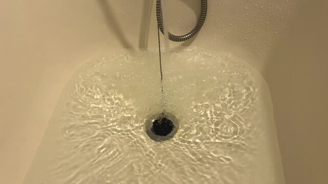 Bathtub filling with running water from a faucet with decorative tiles and wood paneling