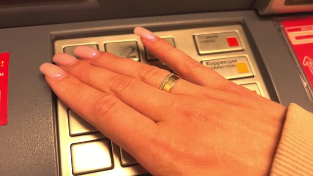 Woman's hand with long nails pressing buttons on an atm keypad during a financial operation