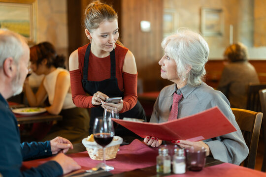 Polite young waitress taking order from elderly couple during relaxed dinner in comfortable restaurant setting