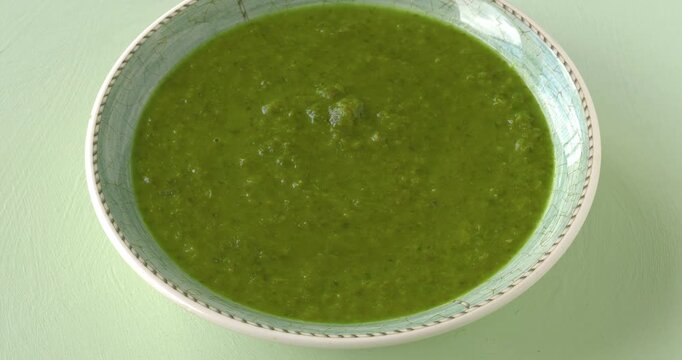 Soup made of romaine lettuce with mint. Pastel green background, table spin.