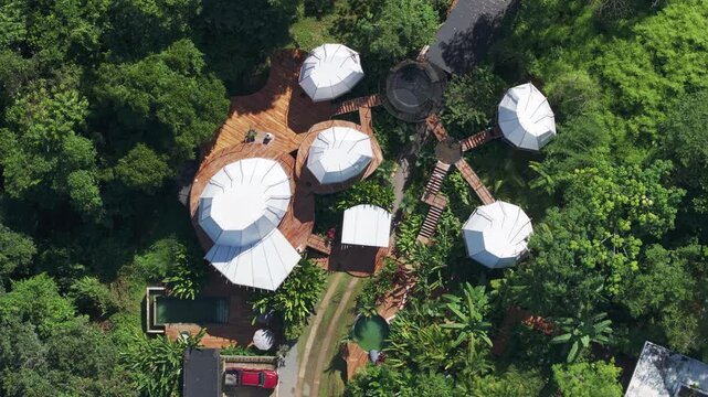Aerial drone footage showcases a stunning villa in Costa Rica featuring white geodesic dome structures connected by wooden decks surrounded by dense tropical jungle with swimming pool visible.