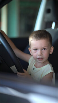 Joyful little boy turns the steering wheel with a big smile, pretending to drive the car. Heartwarming childhood moment inside the vehicle interior.