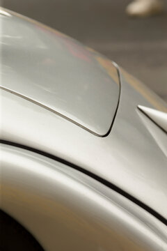 Tight detail of a silver metallic car showing the smooth curved body panel, recessed fuel door, and wheel arch edge. Soft studio lighting highlights the