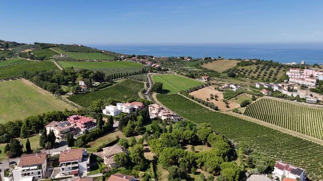Aerial drone view of Roseto degli Abruzzi town residential houses with solar panels near green vineyards and hills by Adriatic sea coast in Italy.