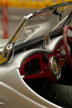 Close-up view of a classic convertible interior showing a polished chrome dashboard, glossy red instrument panel and a textured red steering wheel,