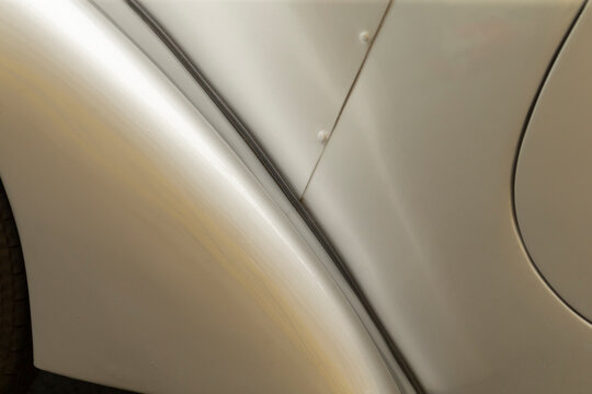 Tight detail view of a silver metallic car showing the curved fender, body panel seam, and smooth painted surface with subtle reflections. Visible rivets