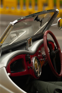 Close-up view of a classic convertible interior showing a red leather-wrapped steering wheel, glossy red and silver dashboard, chrome-trimmed gauges