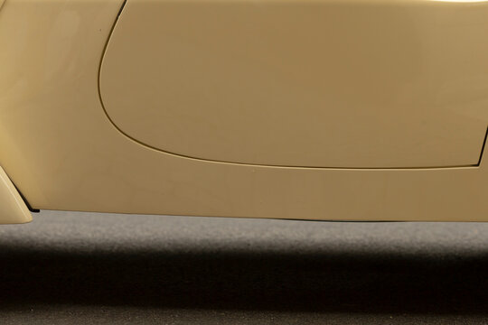 Tight view of a beige car's lower side panel showing the fuel door outline and smooth painted bodywork above a dark textured rocker panel. Soft even lighting