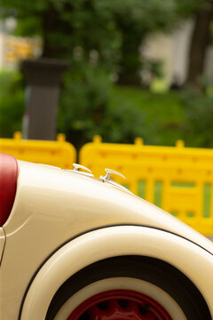 Close-up of the rear section of a cream-colored vintage car showing the curved fender, red leather seat edge and whitewall tire. Soft outdoor daylight