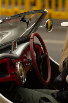 Close-up view of a vintage convertible car interior featuring a textured red steering wheel, chrome instrument dials, and glossy red dashboard trim. Partial