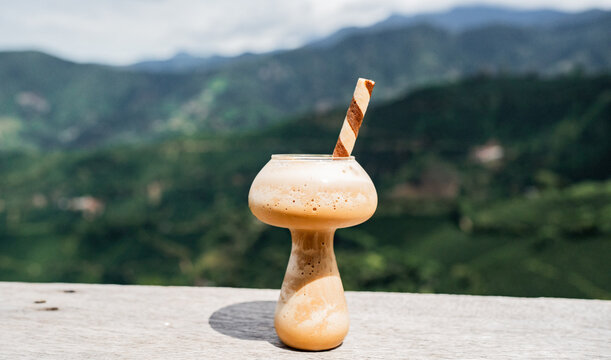 Batido de caf&eacute; helado con espuma servido en copa de vidrio frente a paisaje de monta&ntilde;as