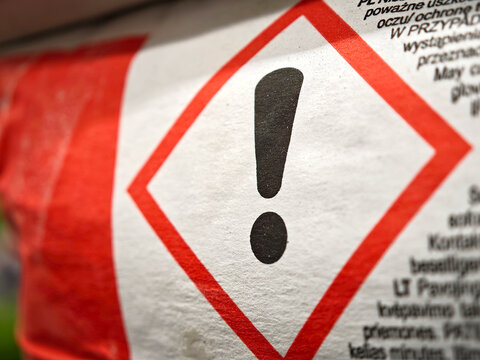 Warning exclamation mark hazard pictogram on industrial product label, macro detail closeup of red diamond GHS safety symbol printed on packaging, chemical regulations and workplace danger concept