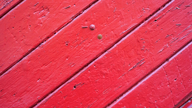 Bright red weathered wooden planks background, closeup of painted boards with diagonal seams, scratches, metal tacks and thick paint texture, rustic damaged abstract surface with copy space, no people