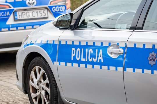 Polish Policja patrol cars parked outside closeup of blue reflective markings on white police vehicle door with second cruiser blurred behind, law enforcement public safety and emergency service scene