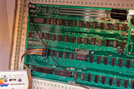 Apple Computer 1 circuit board closeup in museum display, vintage 1976 green motherboard with chips, wires and cassette tape, retro computing history and early personal computer technology, no people.