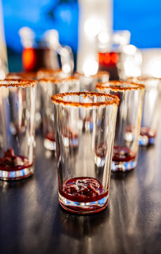Vasos preparados para c&oacute;cteles con escarchado de chile y jarabe de frutos rojos en barra de eventos