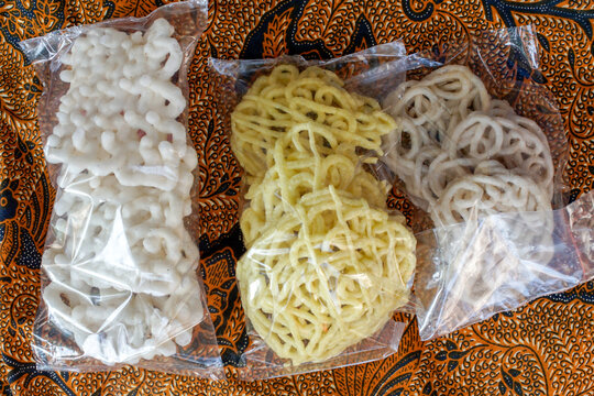 Collection of traditional Indonesian kerupuk crackers individually packed in clear plastic bags on authentic batik fabric. Colorful Asian snack assortment with cultural identity and copy space