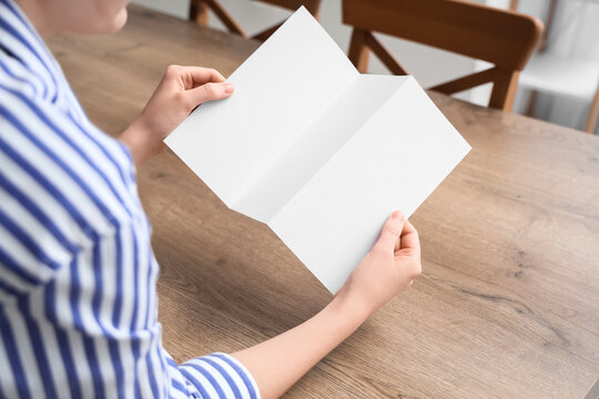Person holding a blank trifold brochure mockup with copy space on a wooden table, marketing and advertising concept, the empty paper template is ready for custom content