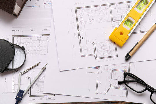 Architectural blueprints with drafting tools, level, and house model for construction and home design planning