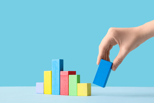 Hand placing a blue wooden block to complete a colorful bar graph, business growth and data analysis
