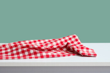 Obraz premium Red and white checkered tablecloth draped on a white table with a teal background, copy space
