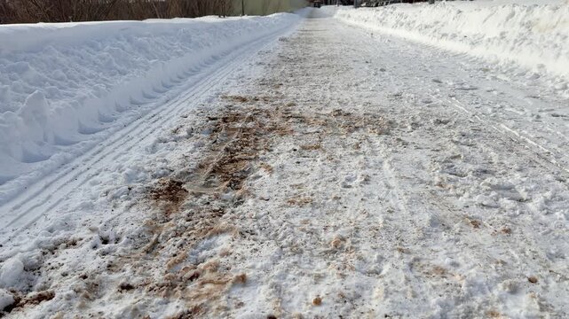 Footprints in snow near fence showing meandering human path along guarded perimeter, adjacent tire tracks suggest vehicle access