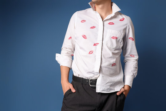 Young man with kiss marks on his shirt against dark blue background