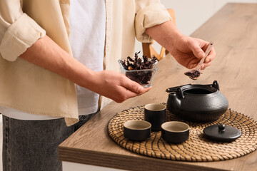 Young man pouring dry hibiscus tea into teapot in kitchen, closeup © Pixel-Shot