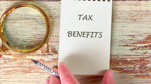 Hands show different writing styles for tax benefits on paper. The table is wooden and the lighting is natural. The activity focuses on writing clearly
