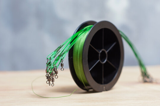 Braided fishing line spool with wire leaders and swivels on wooden surface. Essential terminal tackle for freshwater fishing, angling preparation, tackle retail, outdoor recreation and sport fishing.