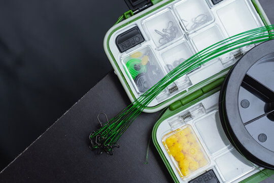 Fishing tackle box with braided line spool, hooks, sinkers and rigs on dark background. Outdoor recreation gear, professional angling equipment or sport fishing banner concept.