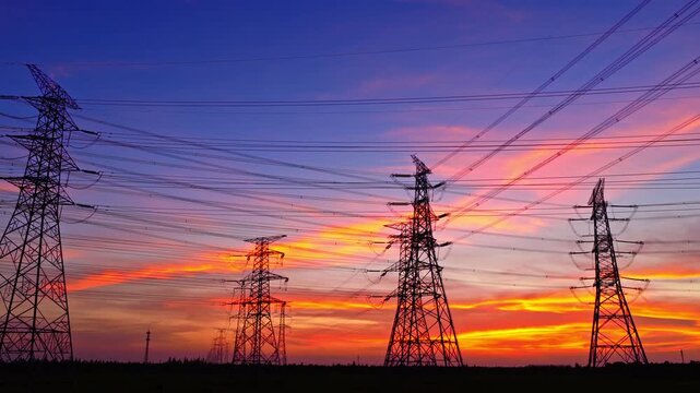 High voltage transmission towers and power lines silhouetted against the sunset sky, depicting the electricity grid and energy industry