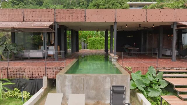 Aerial view of a luxurious modern villa in Costa Rica featuring an infinity pool with waterfall edge and wooden deck surrounded by lush tropical rainforest vegetation and gardens.
