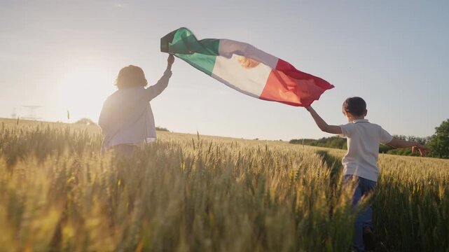 Little children joyfully run through country road waving the Mexican flag, flutters in the warm breeze above yellow wheat fields. Latin American pride and freedom.