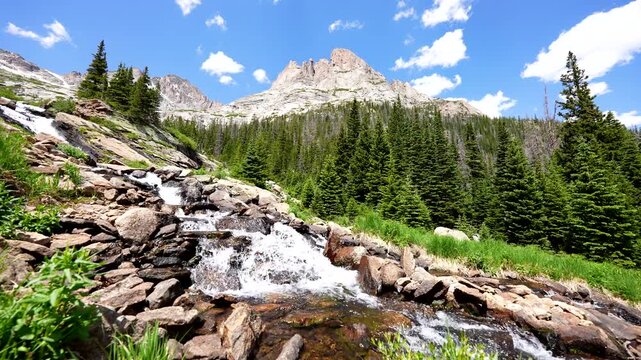 Rocky Mountain National Park river empties from Black Lake in RMNP with rushing water over rocks and boulders with natural sound audio on blue sky and mountains in background