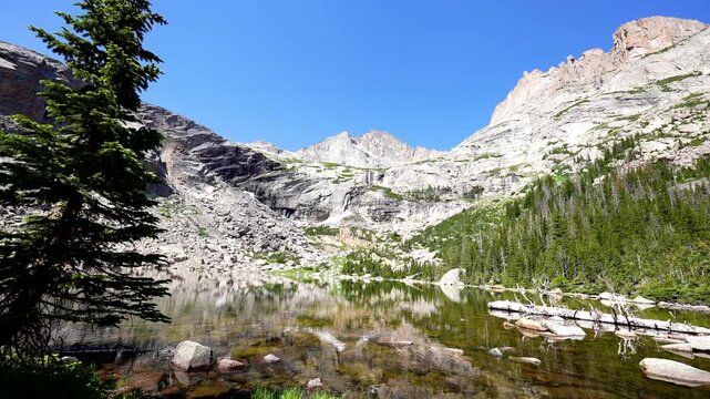 wide shot of beautiful rocky mountain lake in the RMNP colorado rockies Black Lake with reflection on clear glacial water and cloudless blue sky with audio
