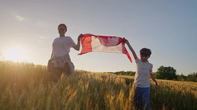 Mother and son run across wheat field holding Canadian flag in warm light. Family bonds, prairie landscapes, agricultural heritage and Canadian national pride