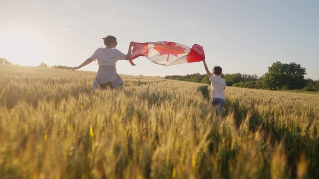 Mother and son run across wheat field holding Canadian flag in warm light. Family bonds, prairie landscapes, agricultural heritage and Canadian national pride