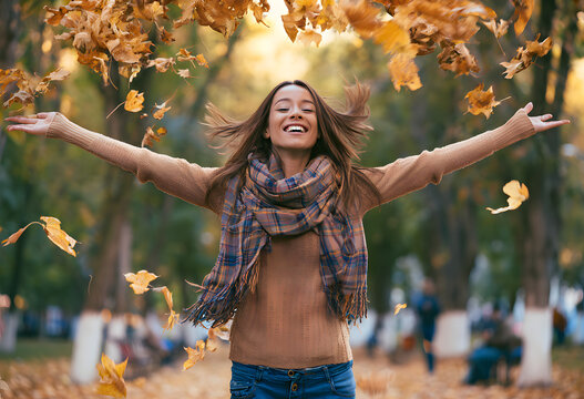 A cheerful woman enjoying tossing leaves at the city park during autumn.