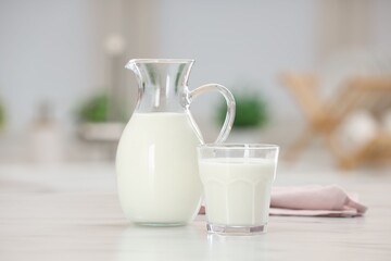 Fototapeta na wymiar Fresh milk in glass and jug on light table indoors