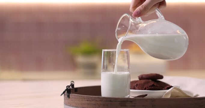 Woman pouring fresh milk into glass at table in kitchen, closeup